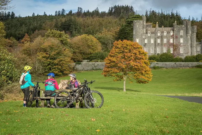 Mountain bikers resting on a bench in Castlewellan Forest Park, with Castlewellan Castle behind them